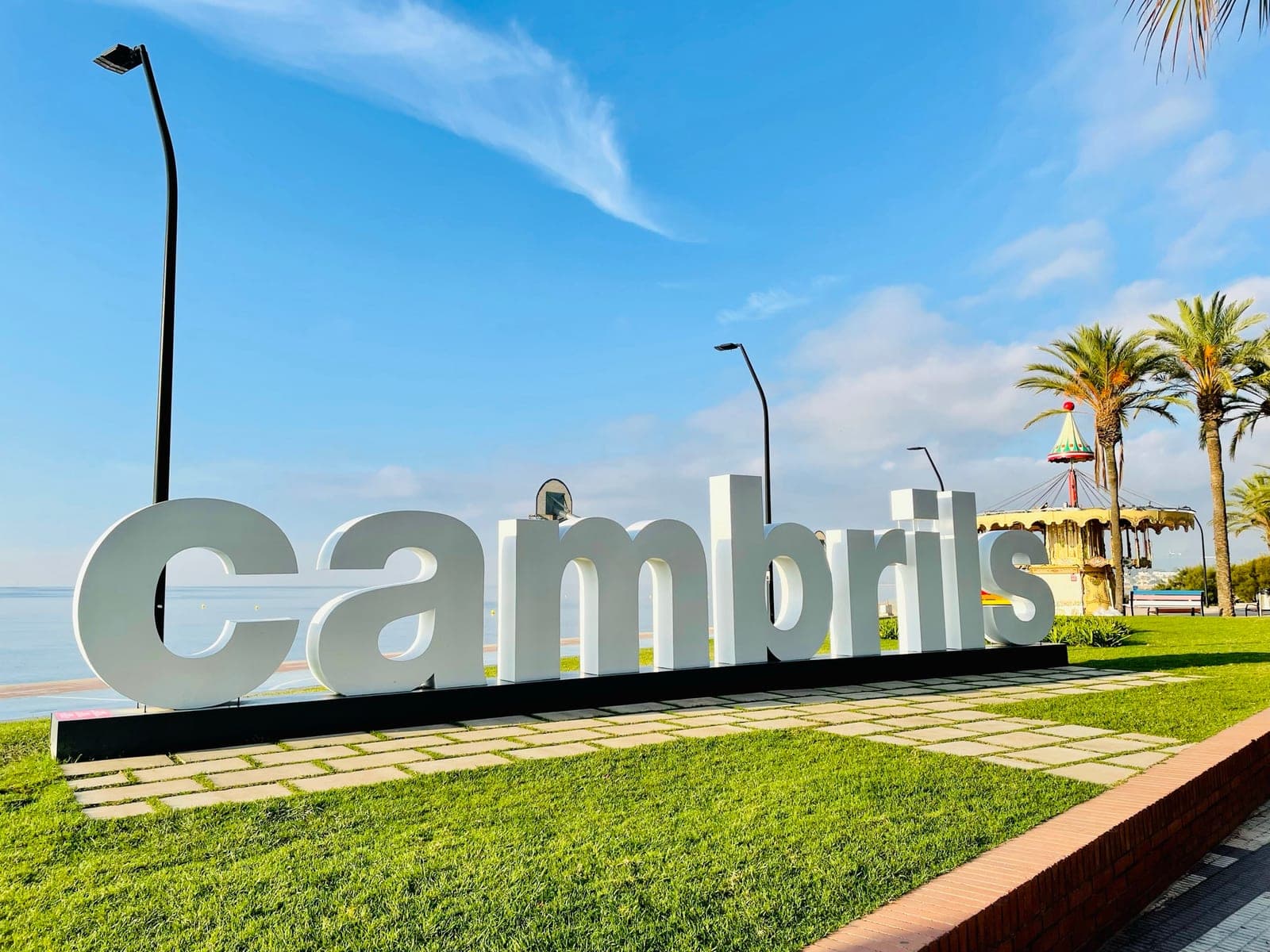 The Cambrils seafront sign, palm trees and the sea behind.