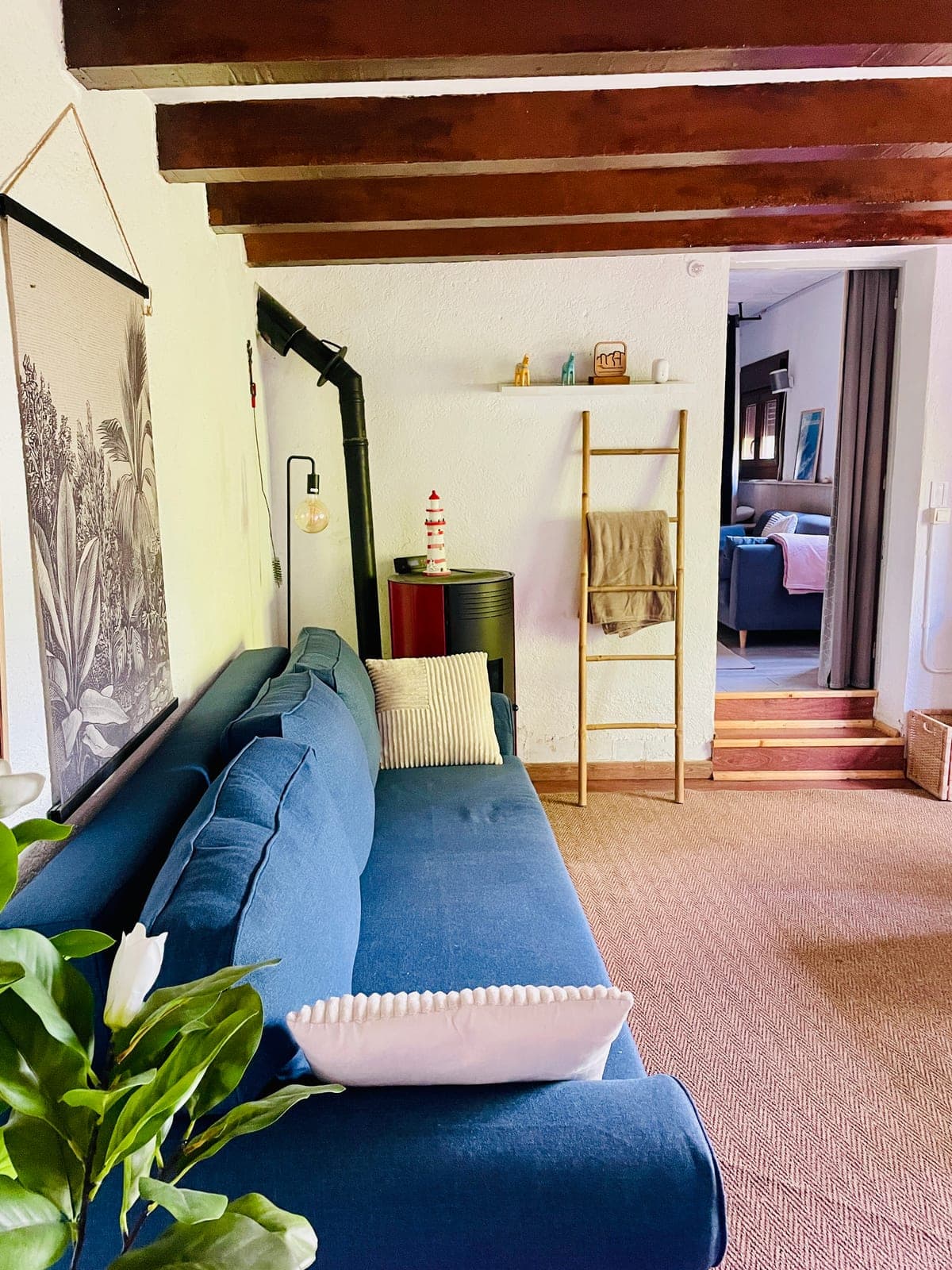 The main house living room: beamed ceilings, blue sofa, and the pellet stove.