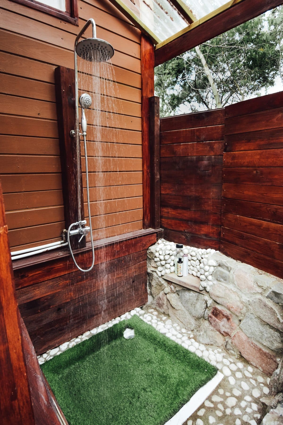 The outdoor shower, running, with cedar walls and a floor of river stones.