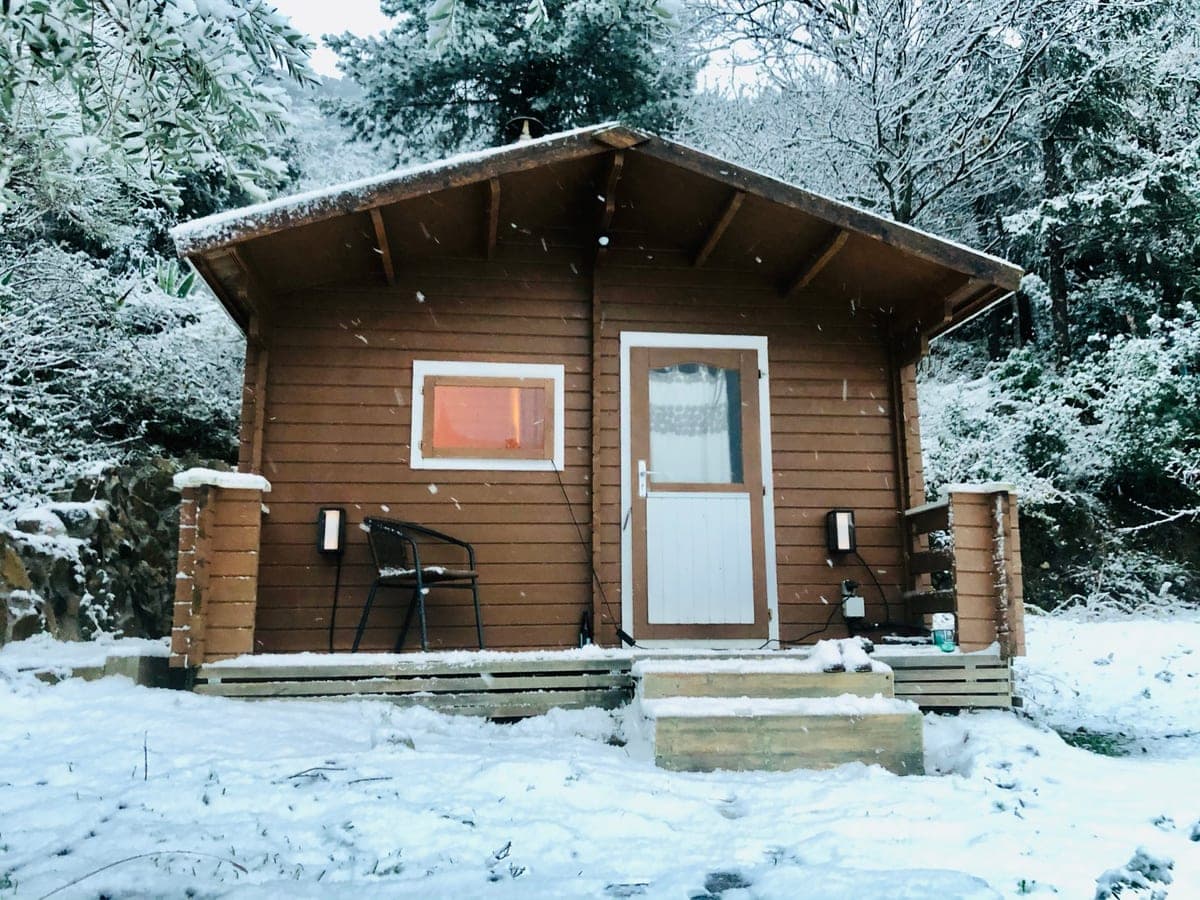 The sauna cabin under a rare snowfall, its window lit.