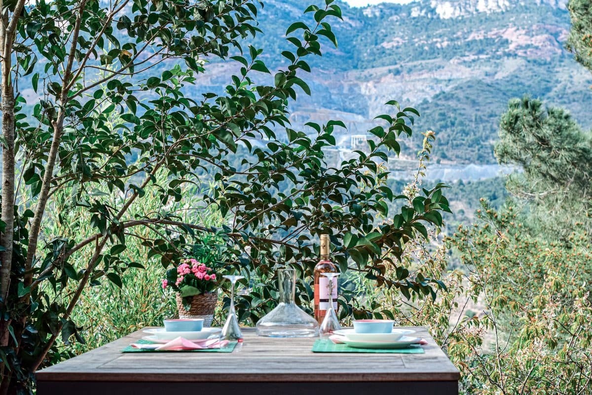 A table laid for two outside, the Montsant ridge filling the background through blossom.