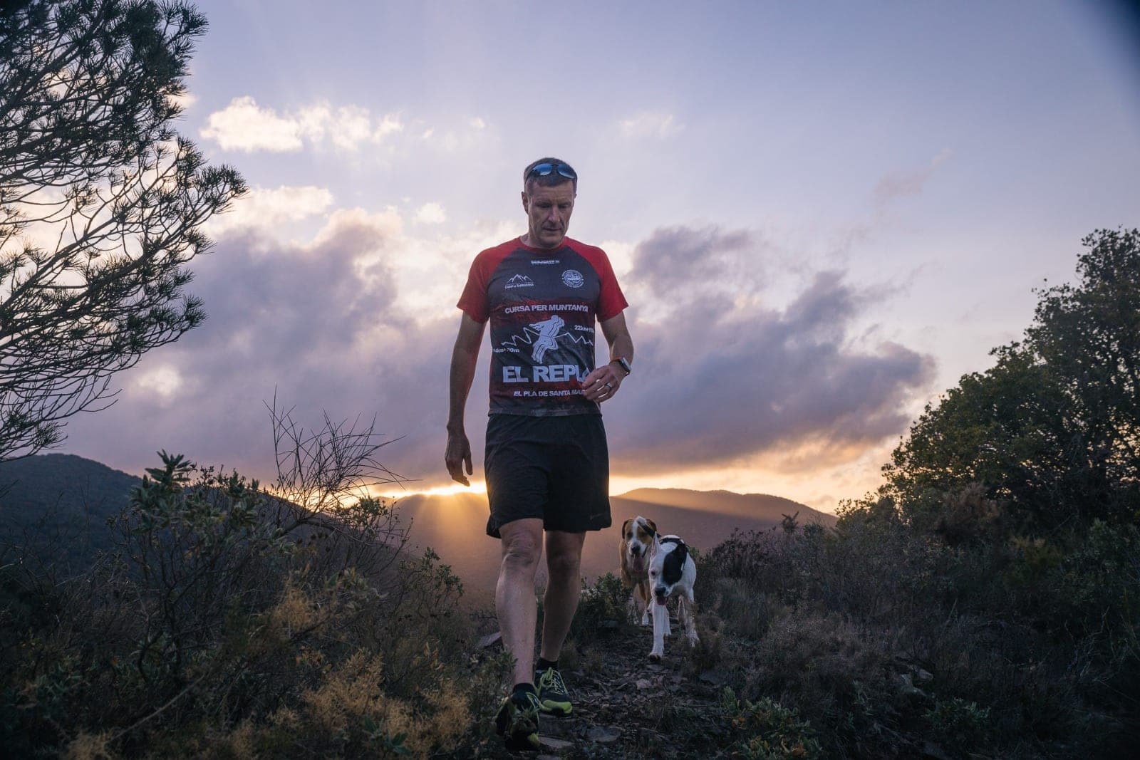 Kai climbing a ridge trail at dusk, two dogs alongside.