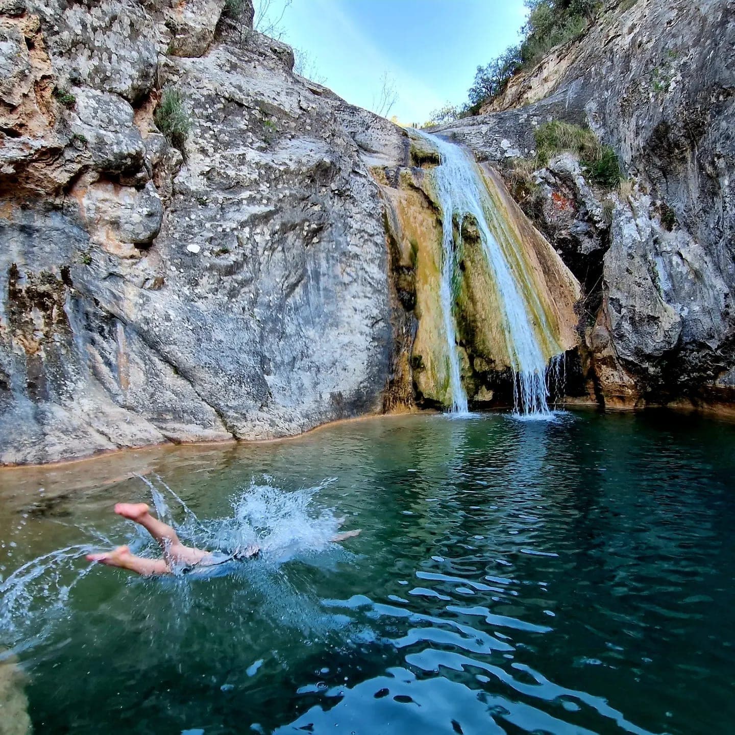 Someone mid-swim in a rock pool below a small waterfall.